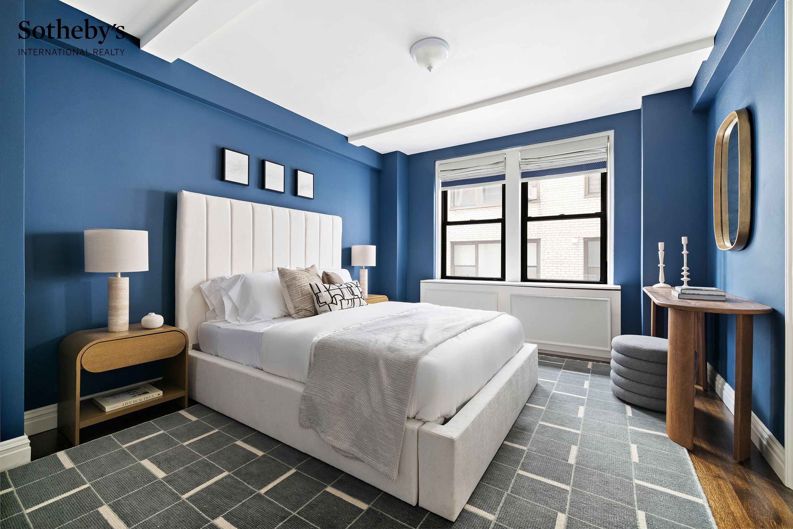 Bedroom with deep blue walls, a white upholstered bed, and a gray grid-pattern rug.