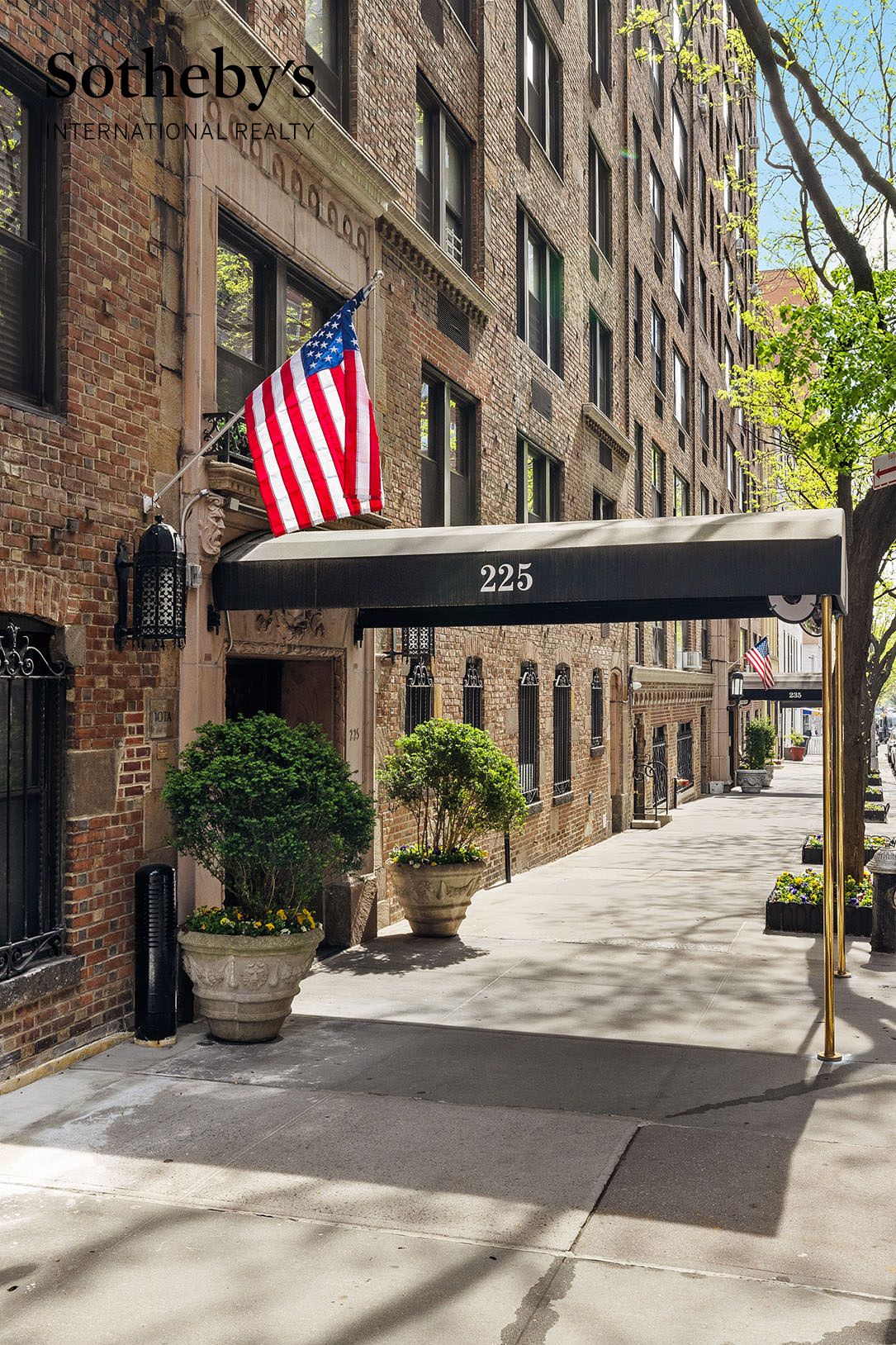 Brick apartment building entrance at 225 East 73rd Street, with an American flag and planters.