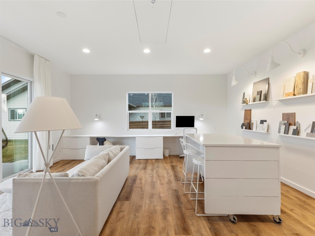 Staged home office with a white sofa, rolling desk, and built-in display shelves.