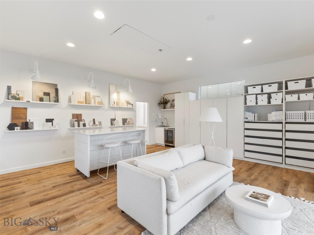 Bright living area with a white sofa, wood floors, and shelves displaying decor samples.