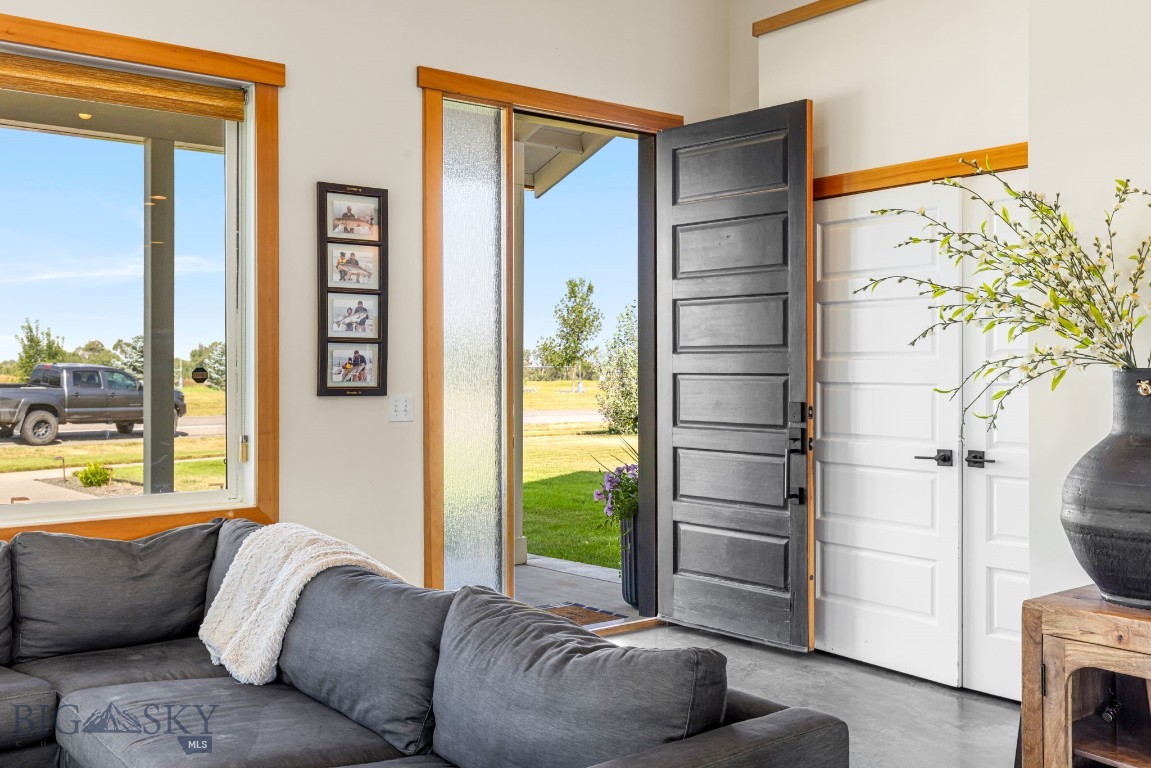Living room with a gray sectional beside an open front door and large wood-trimmed windows.