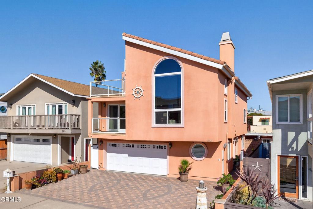 Peach coastal home with a tall arched window, tile roof, and patterned driveway.
