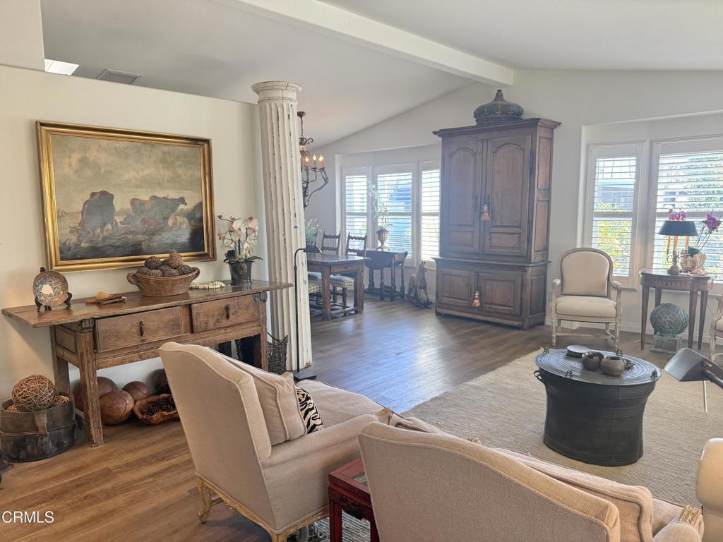 Living room with hardwood floors, antique wood furniture, a classical column, and large shuttered windows.