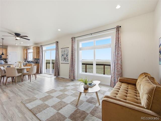 Open-plan living and dining area with a tan sofa and large windows overlooking a deck.