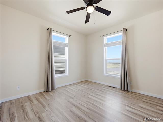 Empty bedroom with two curtained windows, a ceiling fan, and light wood-look flooring.