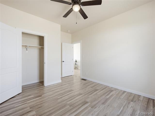 Vacant bedroom with wood-look flooring, ceiling fan, and open closet.