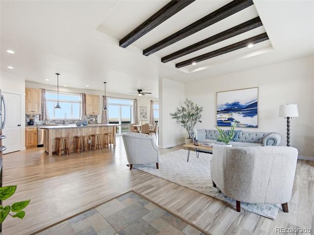 Open-plan living room and kitchen with a large island, upholstered seating, and exposed ceiling beams.