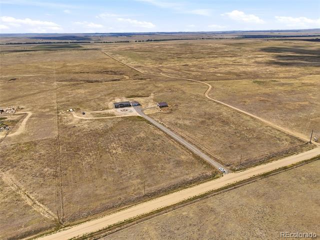 Aerial view of a rural property with scattered buildings and a long driveway across open land.