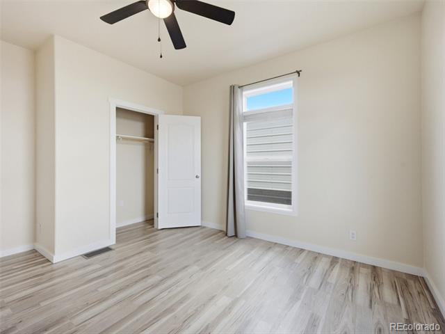 Vacant bedroom with light wood-look floors, a black ceiling fan, and an open closet.