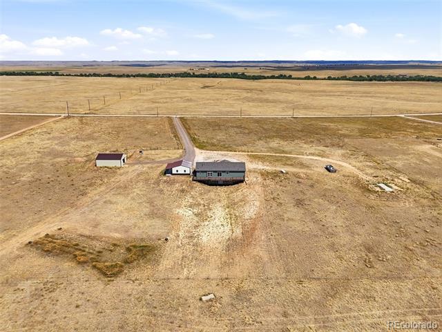 Aerial view of a rural home and outbuildings on dry open acreage.