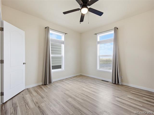 Vacant bedroom with light wood-look flooring, two curtained windows, and a ceiling fan.