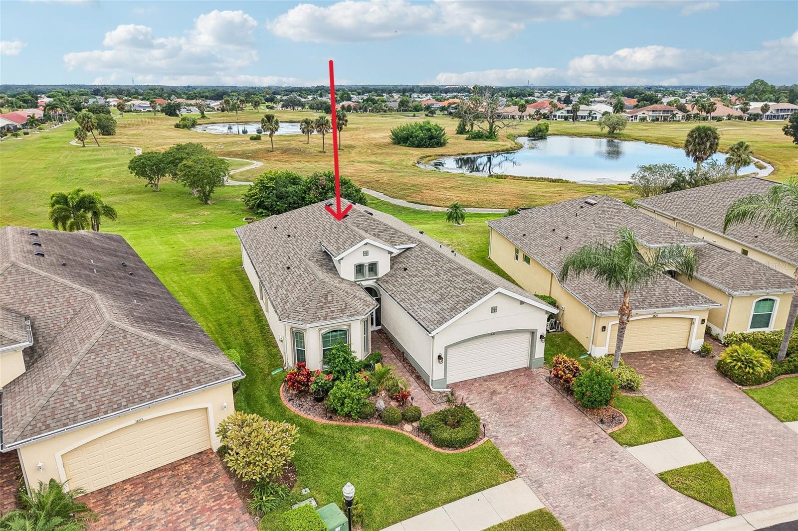 Aerial view of a light-colored home marked by a red arrow, beside community ponds and walking paths.