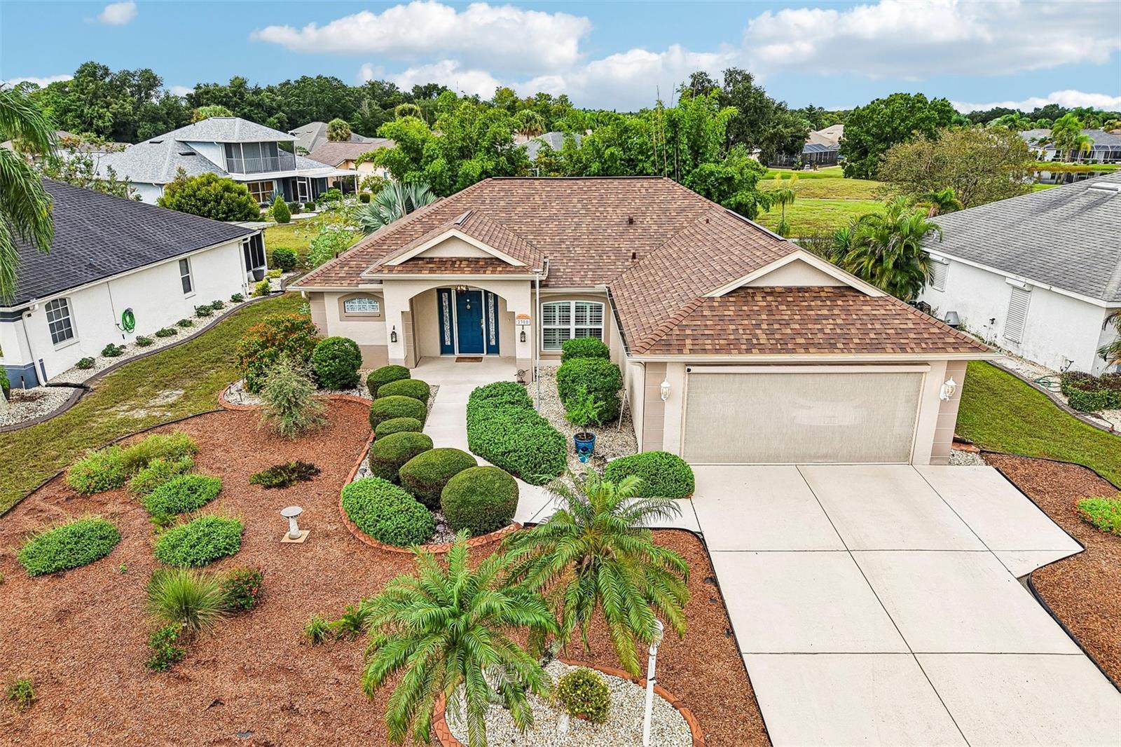 Aerial view of a beige home with a blue front door, attached garage, and landscaped yard.
