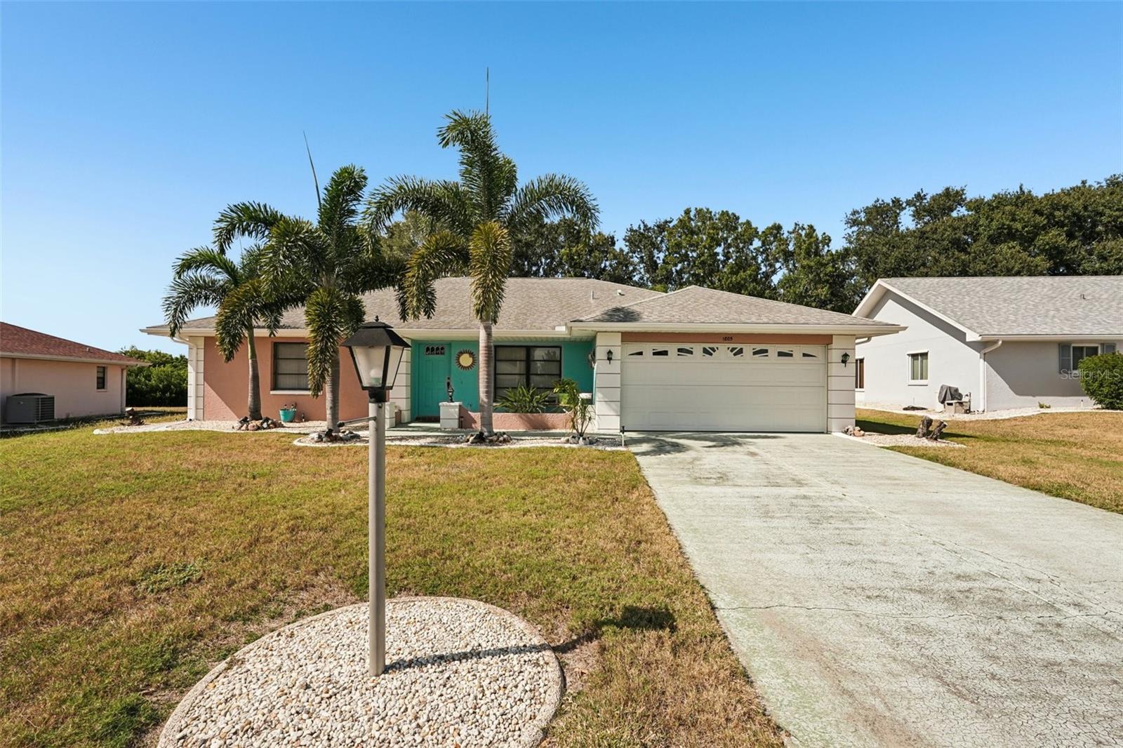 Single-story home with a turquoise front door, palm trees, and an attached two-car garage.