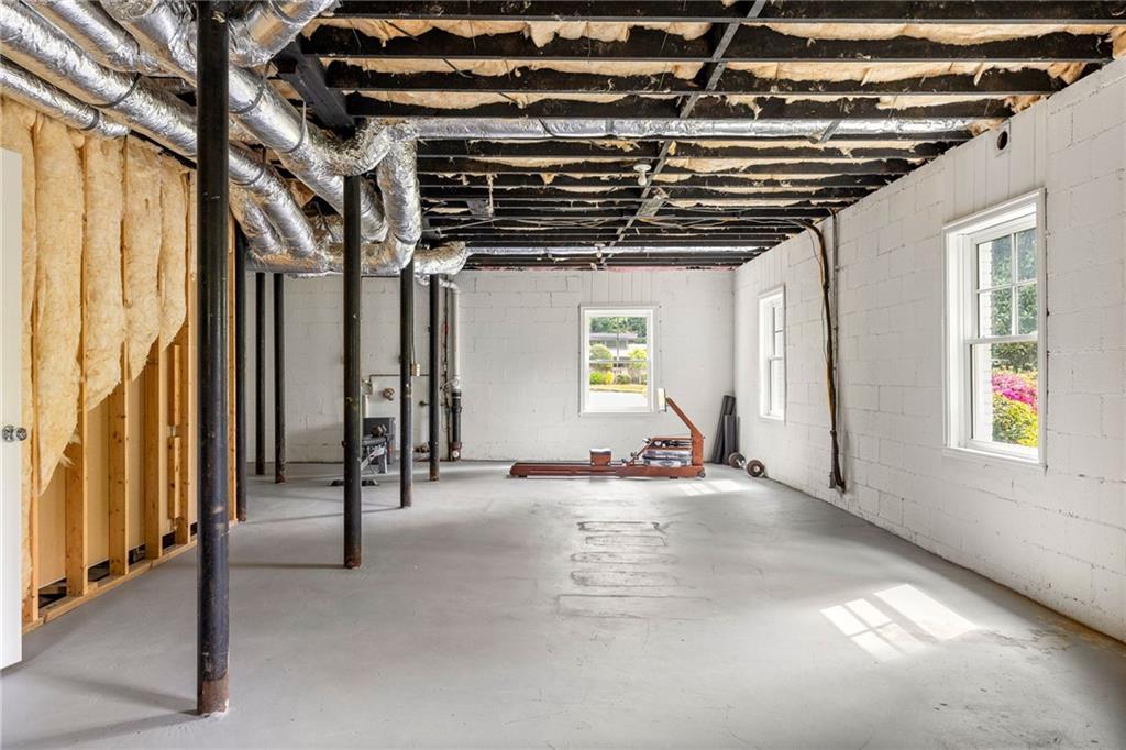Unfinished basement with exposed ceiling joists, ductwork, concrete floor, and windows.