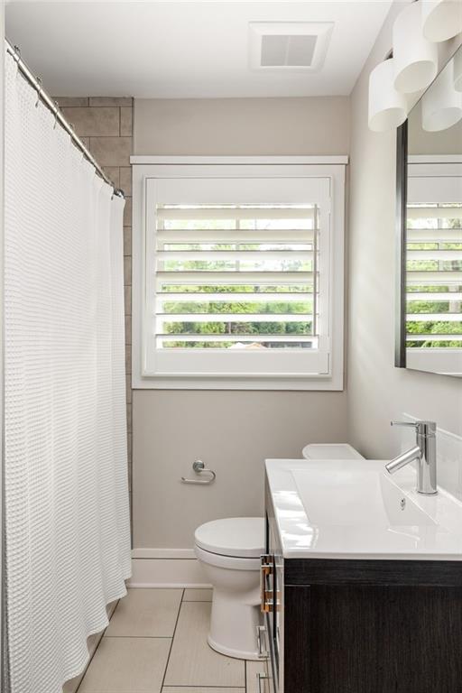 Bathroom with a dark wood vanity, white countertop, tiled shower wall, and shuttered window.