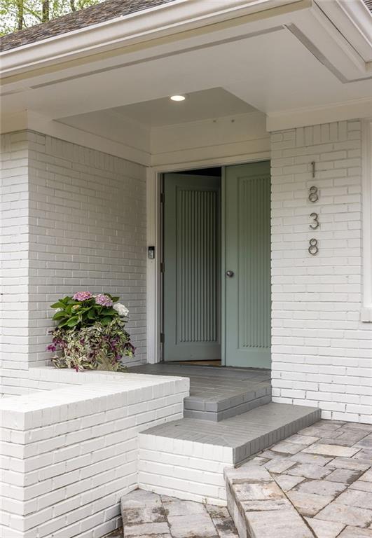 Front entrance with a muted green double door, white brick, tiled steps, and a flowering planter.