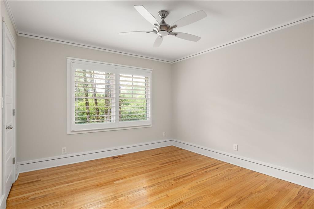 Unfurnished room with hardwood floors, a ceiling fan, and a wide shuttered window.