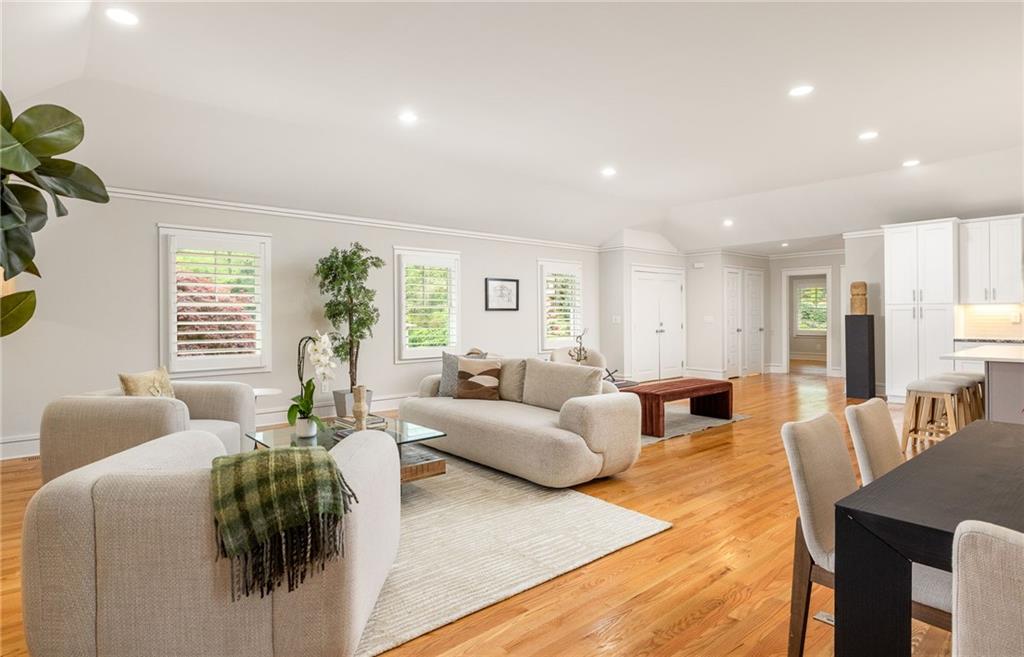 Open-plan living room with light sofas, hardwood floors, and a white kitchen.