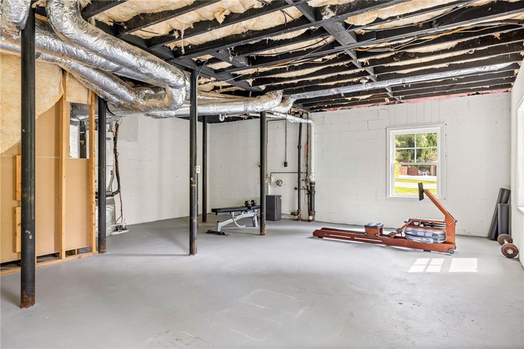 Unfinished basement with exposed ceiling joists, ductwork, concrete floor, and exercise equipment.