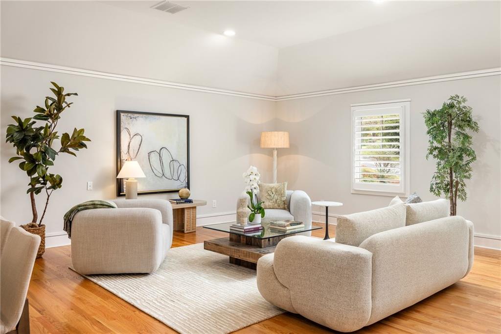 Bright staged living room with cream seating, abstract art, hardwood floors, and a large window.