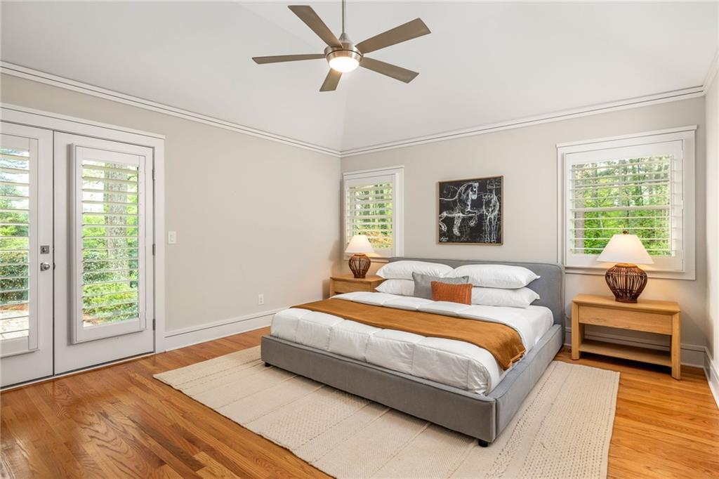 Staged bedroom with a gray bed, rust-colored throw, hardwood floors, and plantation-shuttered windows.