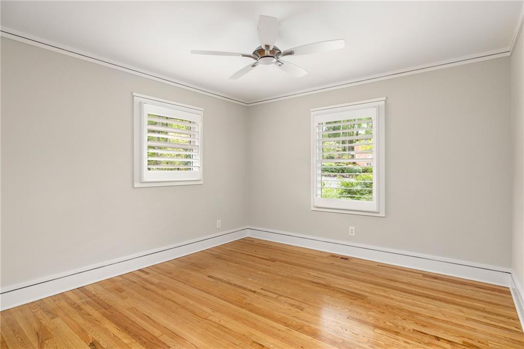 Empty room with hardwood floors, two shuttered windows, and a ceiling fan.