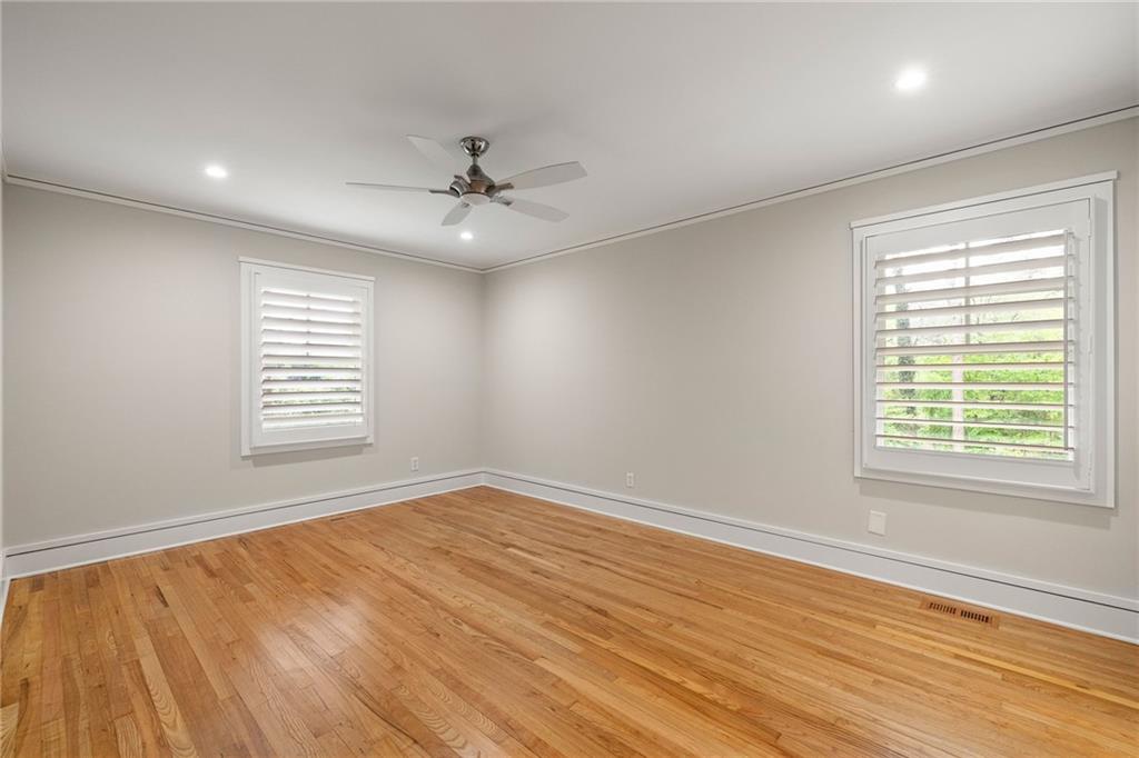 Empty room with hardwood floors, plantation shutters, and a ceiling fan.
