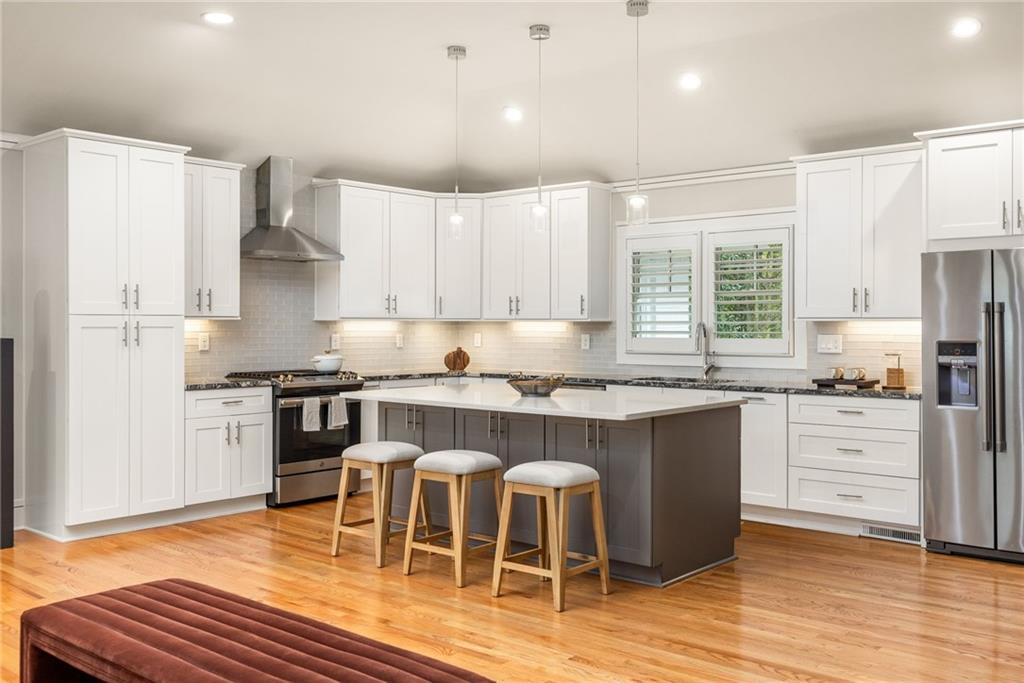 Kitchen with a large dark island, three stools, white cabinets, and hardwood floors.