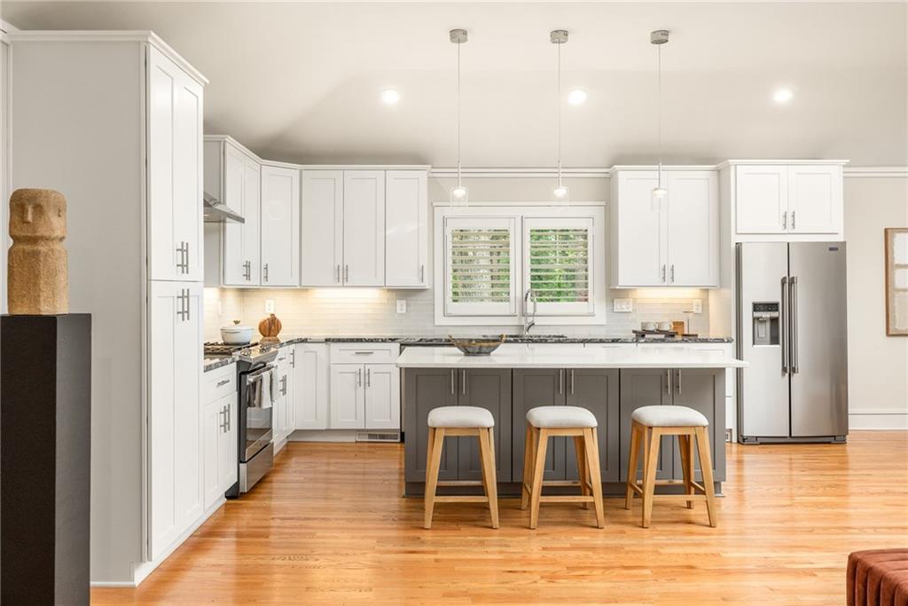 Kitchen with white cabinets, a gray island, three stools, and stainless steel appliances.