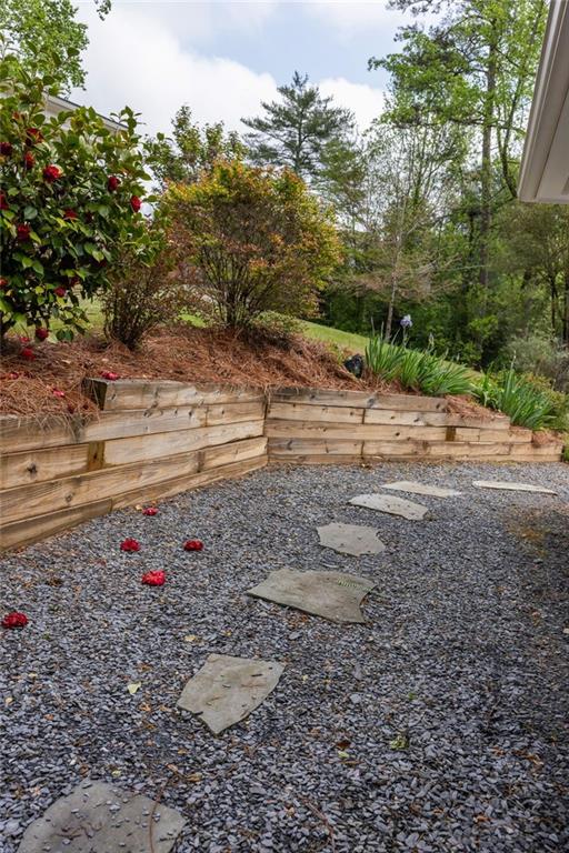 Gravel backyard patio with stepping stones, curved wooden retaining wall, and flowering garden beds.