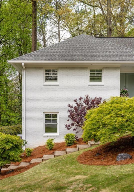 White brick house exterior with landscaped shrubs and stone steps on a sloping lawn.