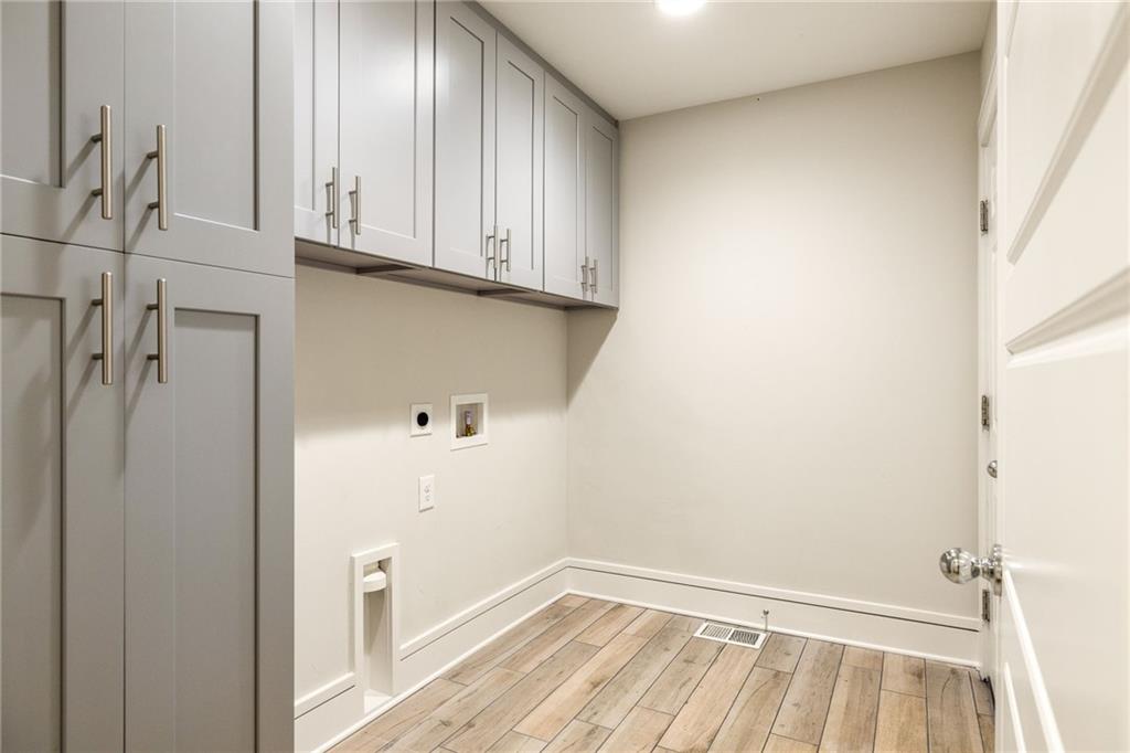 Laundry room with gray built-in cabinets, appliance hookups, and wood-look plank flooring.