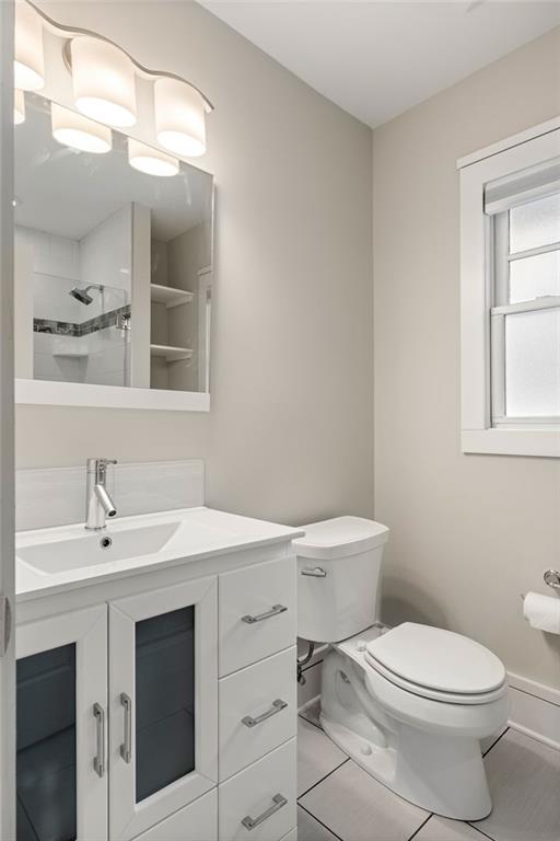 Bathroom with a white vanity, dark cabinet panels, and a window beside the toilet.