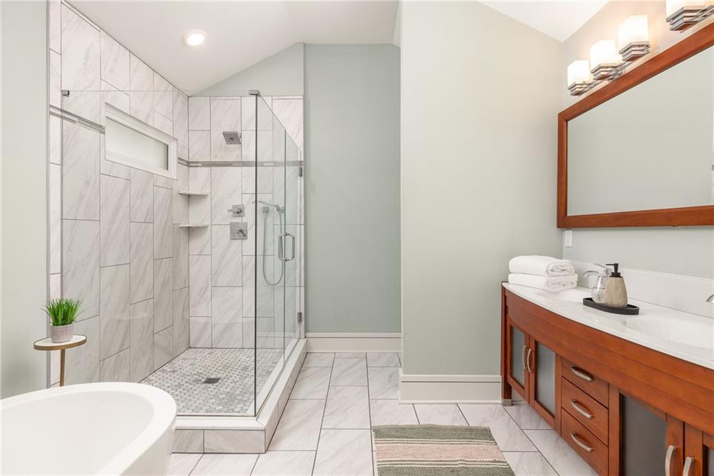 Bathroom with a marble-look glass shower, freestanding tub, and warm wood vanity.