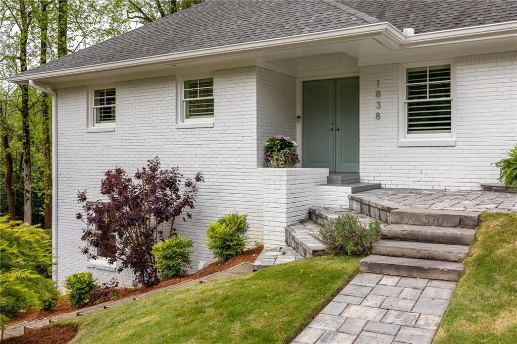 White brick house with green double doors, stone steps, and a landscaped front walkway.
