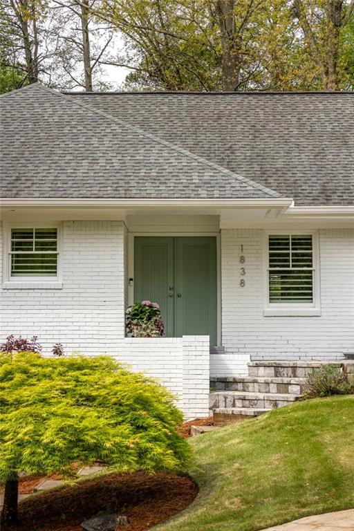 White brick house with green double doors, stone steps, and landscaped front yard.