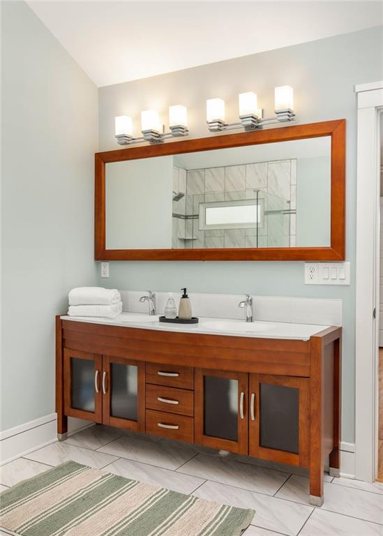 Bathroom vanity with a reddish wood cabinet, wide framed mirror, and four illuminated wall lights.
