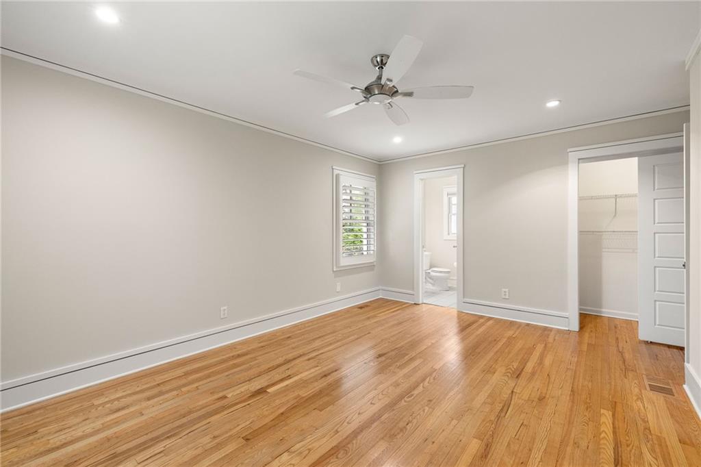 Empty bedroom with hardwood floors, a ceiling fan, and doorways to a bathroom and closet.