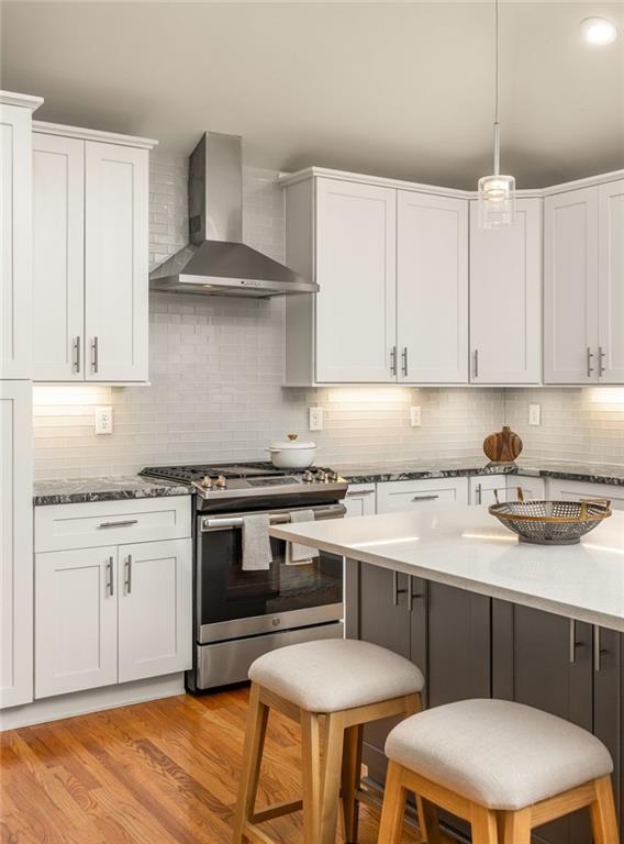 Kitchen with white cabinetry, stainless steel range, and a large island with two stools.