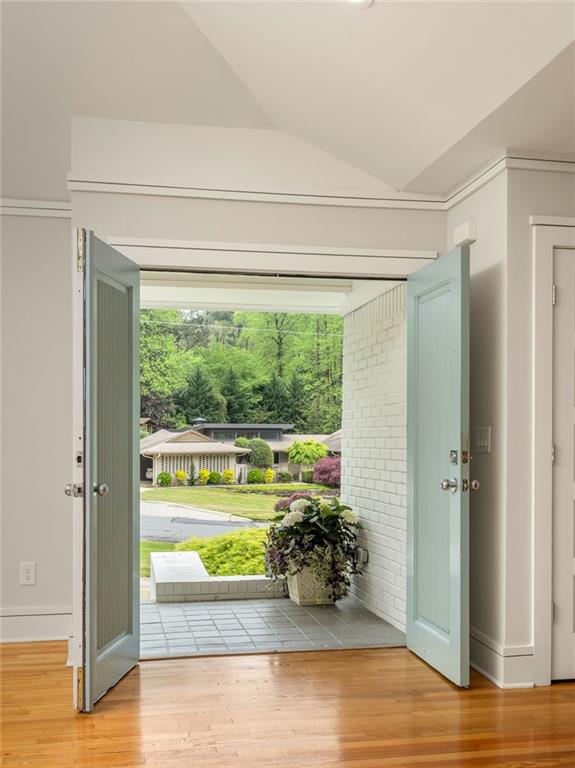 Entryway with open pale blue double doors, polished hardwood floors, and a view of the green street outside.