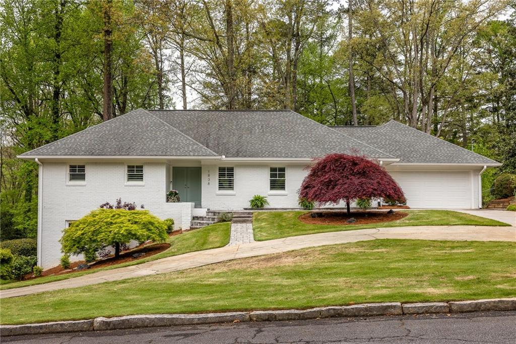 White brick house with an attached garage, sloped driveway, and red Japanese maple in the front yard.