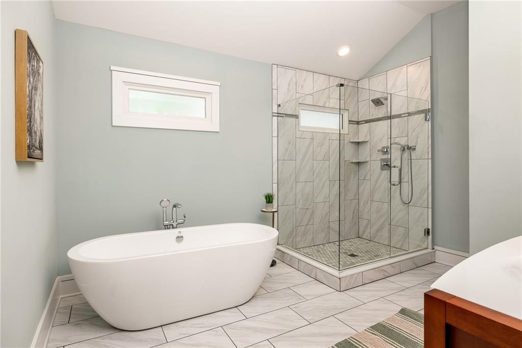 Bathroom with a freestanding soaking tub and glass-enclosed marble-look tiled shower.
