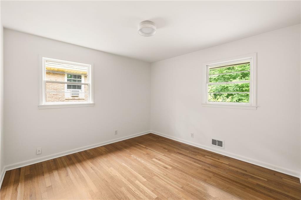 Empty room with hardwood floors and two windows overlooking a brick house and trees.