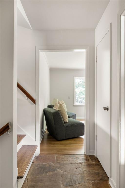 Hallway with rustic stone flooring opens onto a sitting area with a dark sofa and bright window.