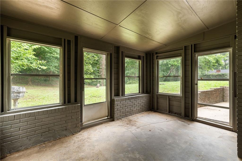 Empty enclosed porch with brick half-walls, concrete floor, and windows overlooking a green yard.