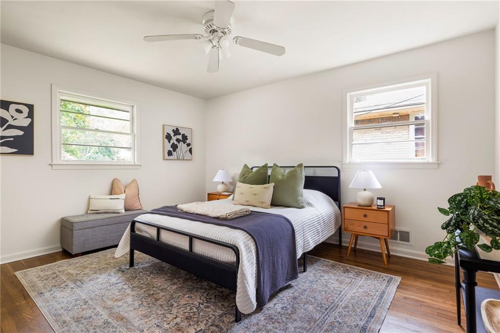 Staged bedroom with a black metal bed, two windows, and a gray bench.