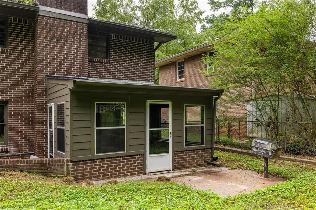 Rear of a two-story brick house with an olive-green enclosed addition and concrete patio.
