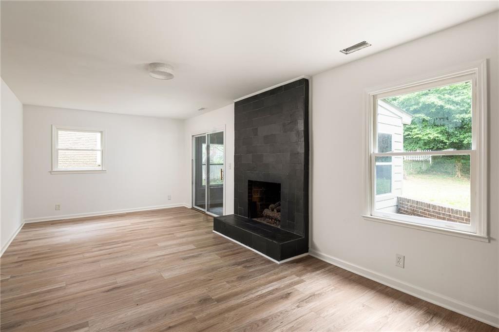 Empty living room with a black tiled fireplace, light wood-look flooring, and windows overlooking the yard.
