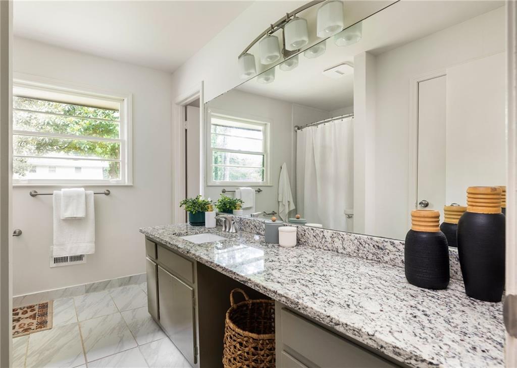 Bathroom with a long granite vanity, large mirror, and window beside the shower.